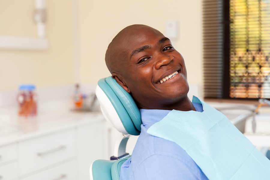 Black man smiles with a blue bib while sitting in the dental chair after a root canal