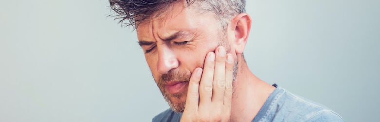 Middle-aged man cringes in pain and touches his cheek due to a traumatic dental injury